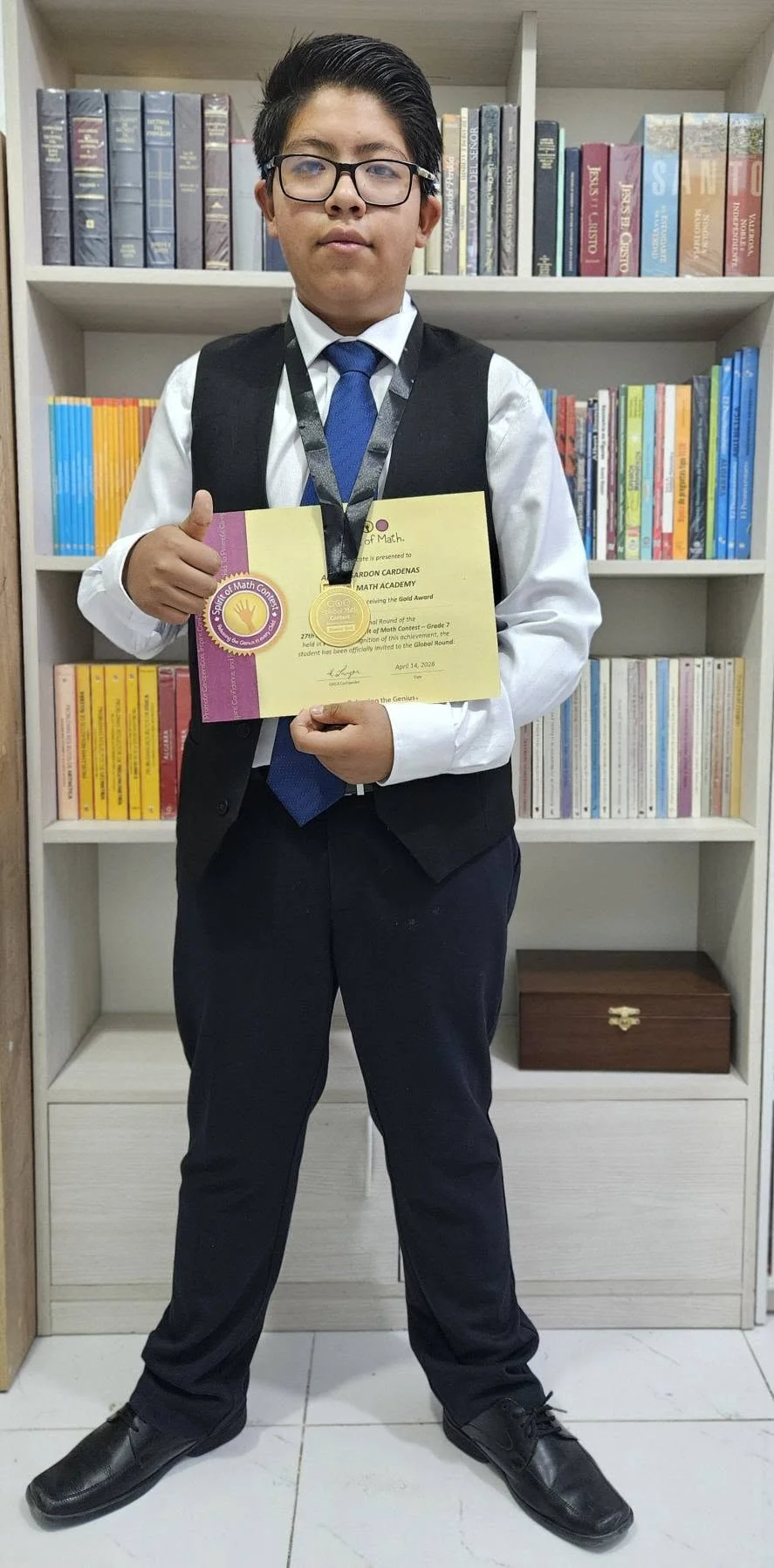 Albert con una medalla y un diploma Gold Award de Spirit of Math, frente a una biblioteca.