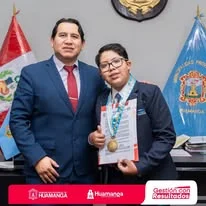 Albert con medallas y un documento, junto a otra persona en un espacio institucional.