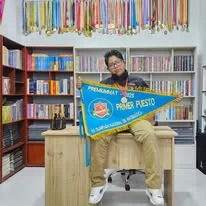 Albert sostiene un banderín de primer puesto frente a una biblioteca y una colección de medallas.