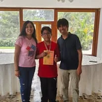Albert muestra una medalla y un documento mientras posa junto a dos personas.