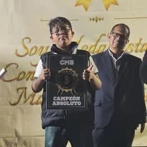 Albert sostiene un reconocimiento con el texto Campeón absoluto junto a otra persona.