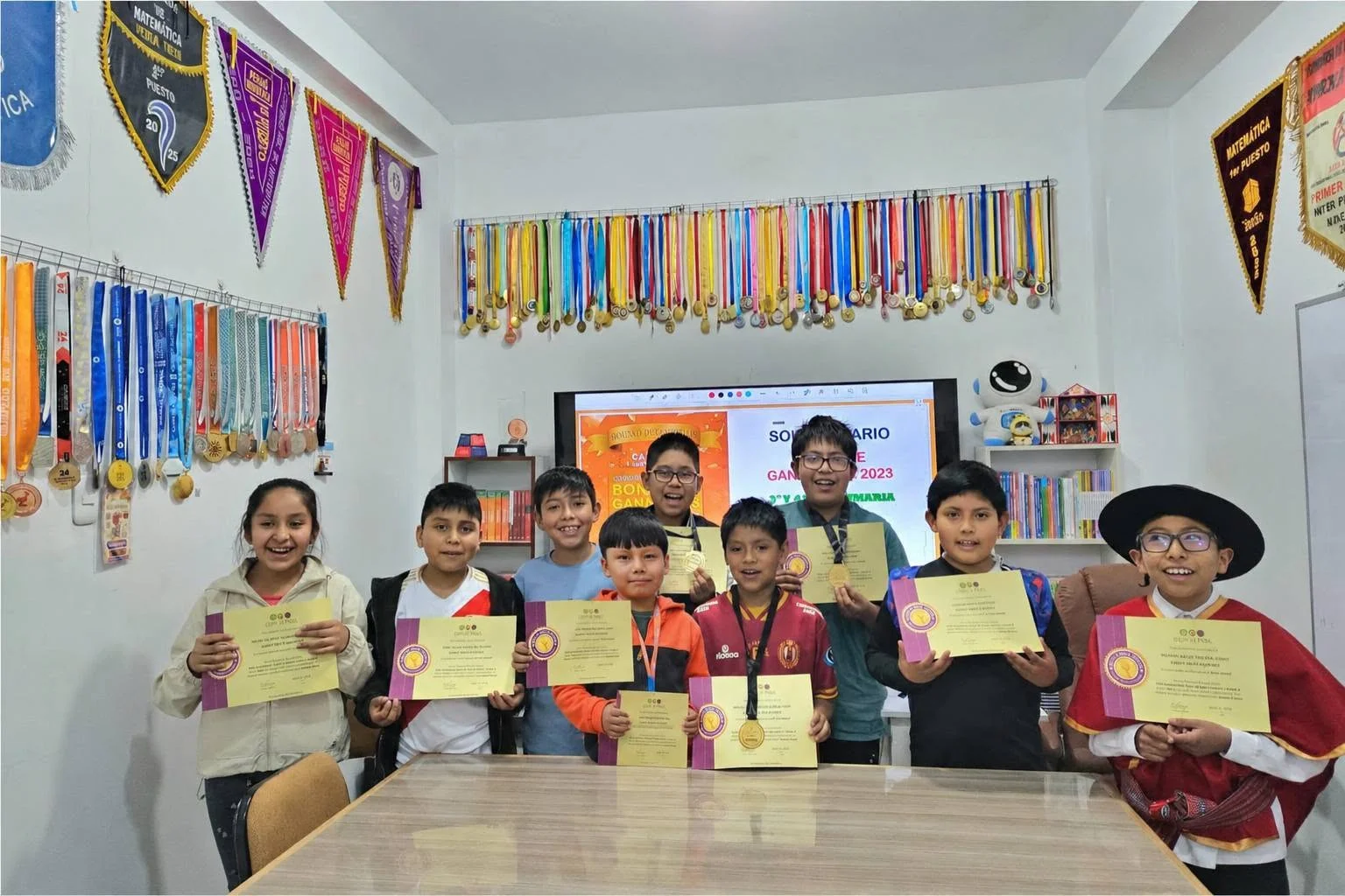 Grupo de estudiantes mostrando diplomas y medallas en el aula